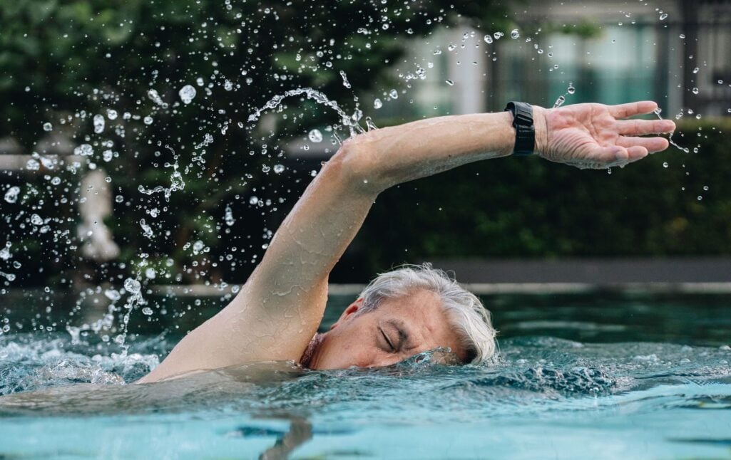 An older man swims laps in an outdoor pool, illustrating how regular physical activity supports brain health and offers a strategy for how to stay mentally sharp as you age.