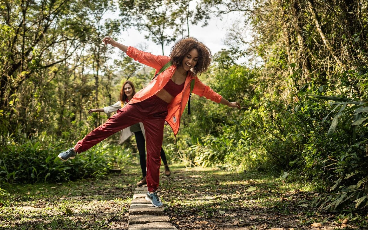 A woman playfully balances on a stone path in a lush forest, representing how balanced funds provide easy stability during the saving years, though retirees must later plan for more flexible withdrawal strategies.