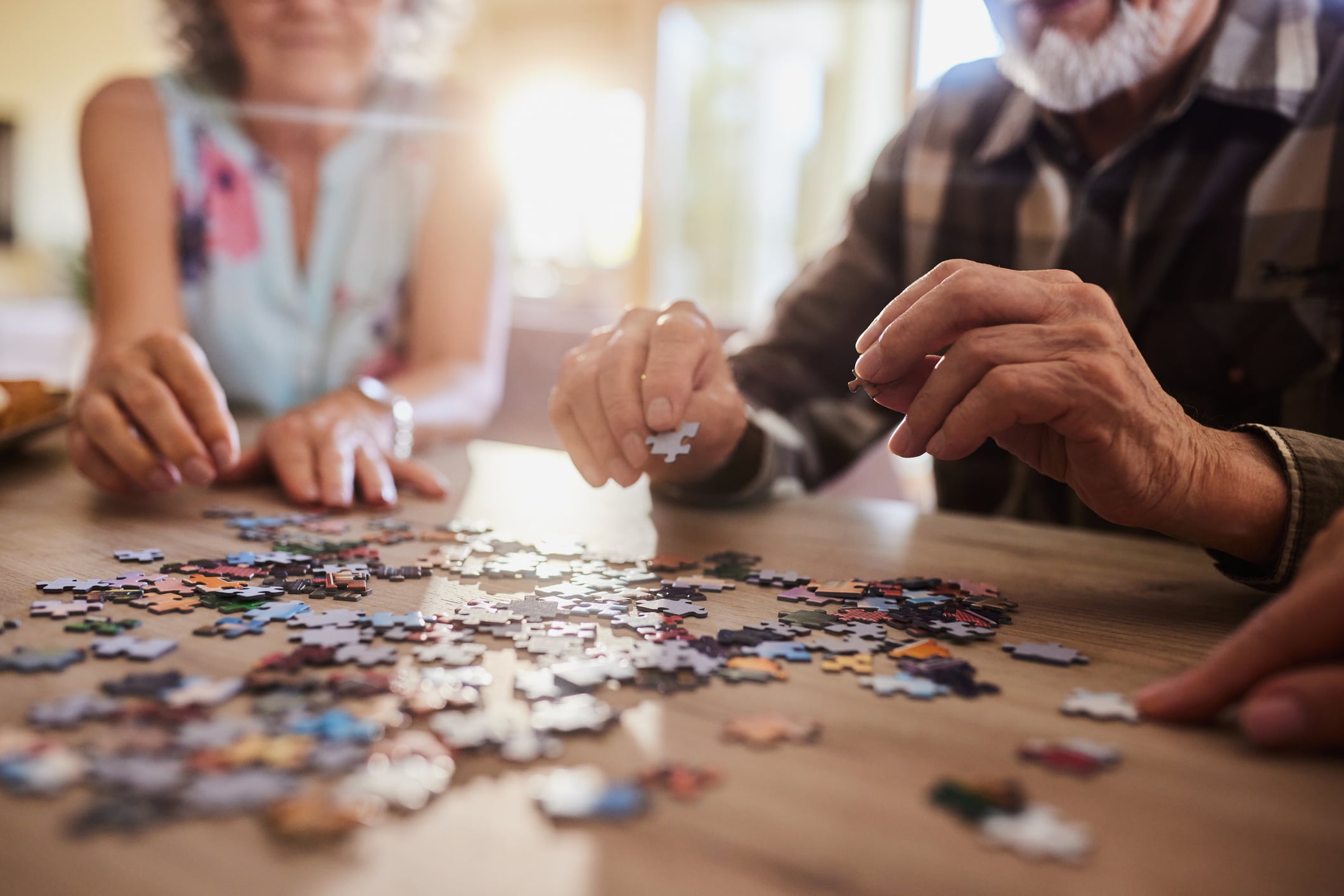 Close-up on the hands of an older couple assembling a jigsaw puzzle together at a table, symbolizing how fitting the right pieces together, like the Vanguard Target Retirement Lifetime Income strategy, helps create a complete and stable retirement picture.